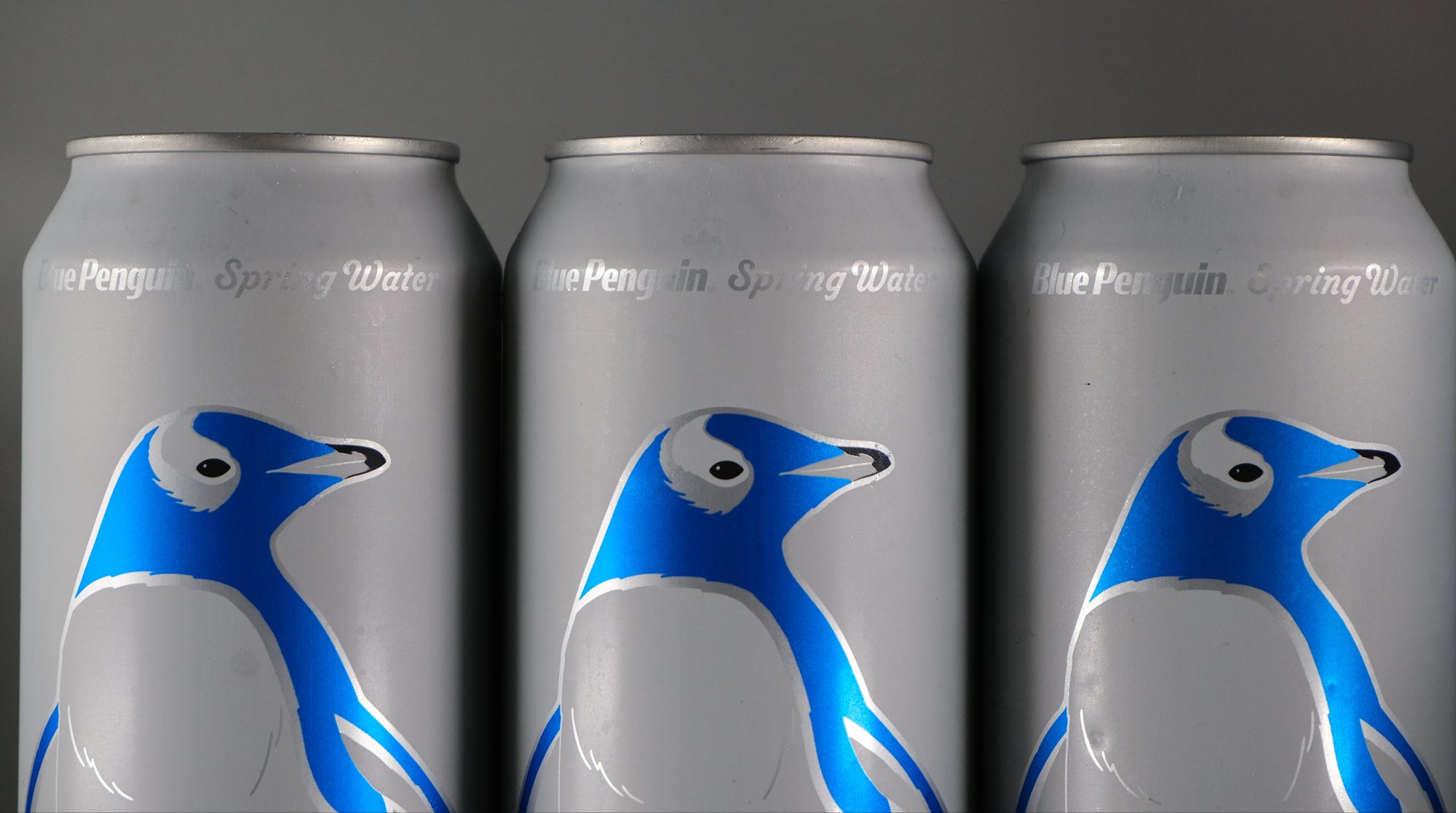 Three cans of Blue Penguin Spring Water with penguin design on a dark background